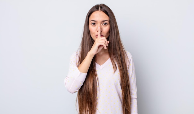 Spaanse mooie vrouw die er serieus uitziet en kruist met de vinger tegen de lippen gedrukt die stilte of stilte eist en een geheim bewaart