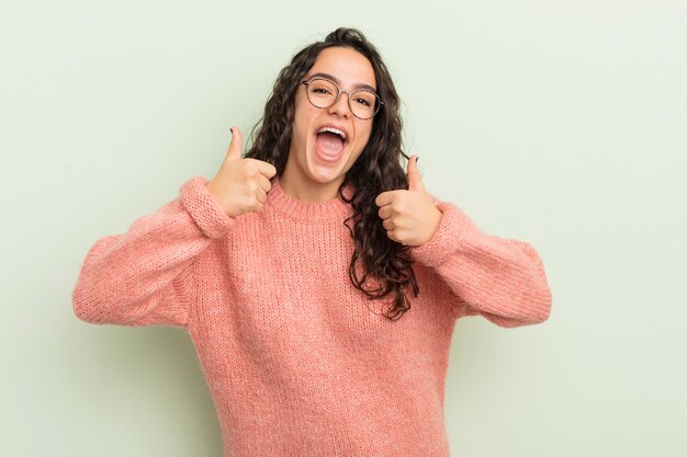 Spaanse mooie vrouw die in het algemeen lacht en er gelukkig positief zelfverzekerd en succesvol uitziet met beide duimen omhoog