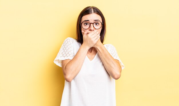 Spaanse mooie vrouw die mond bedekt met handen met een geschokte, verbaasde uitdrukking, een geheim houdt of oeps zegt