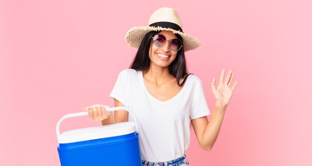 Spaanse mooie vrouw die vrolijk lacht, met de hand zwaait, je verwelkomt en begroet met een draagbare picknickkoelkast