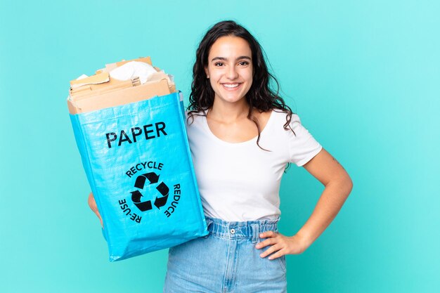 Spaanse mooie vrouw die vrolijk lacht met een hand op de heup en zelfverzekerd en een zak van gerecycled papier vasthoudt