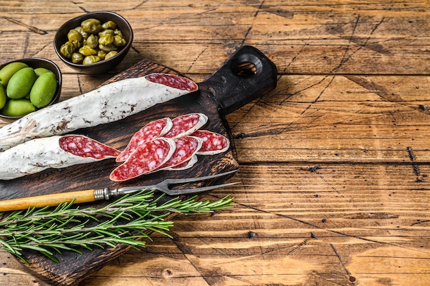 Spaanse tapas Fuet Salami worst plakjes met olijven en rozemarijn op een houten bord op houten tafel. Bovenaanzicht.