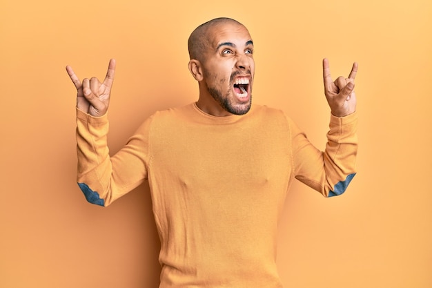 Spaanse volwassen man doet rockgebaar over gele achtergrond boos en boos schreeuwend gefrustreerd en woedend, schreeuwend van woede. woede en agressief concept.