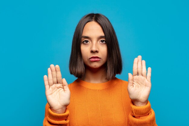 Spaanse vrouw die er serieus, ongelukkig, boos en ontevreden uitziet en de toegang verbiedt of stop zegt met beide open handpalmen