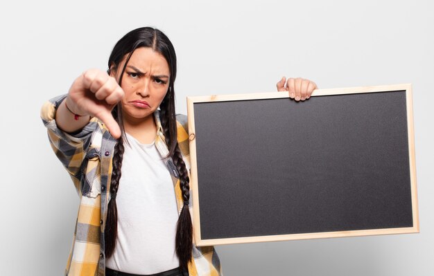 Spaanse vrouw die zich boos, boos, geïrriteerd, teleurgesteld of ontevreden voelt, duimen naar beneden toont met een serieuze blik