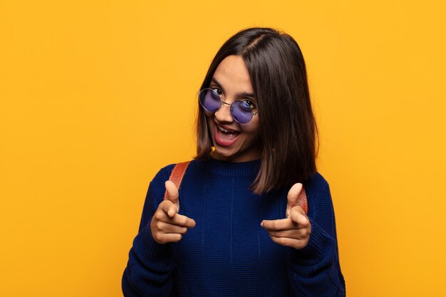 Spaanse vrouw lachend met een positieve, succesvolle, gelukkige houding wijzend naar de camera, pistool teken met handen maken