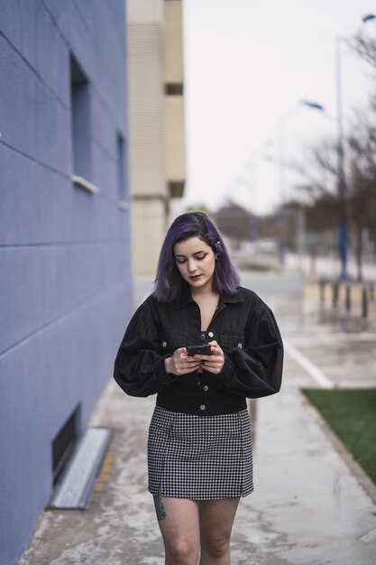 Spaanse vrouw met paars haar die naar haar telefoon kijkt - online communicatie