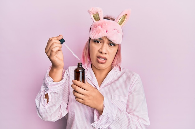 Spaanse vrouw met roze haar in pyjama met nachtserum zonder idee en verwarde uitdrukking. twijfel concept.