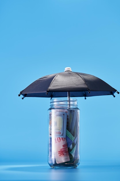 Spaarpot wordt gevuld met valutaschaduw door paraplu tegen blauwe achtergrond