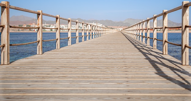 The space is a beautiful long wooden pier among the ocean and mountains.