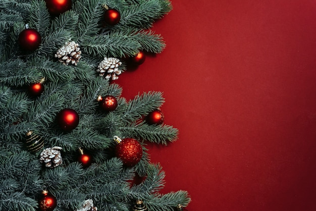 Space for text between Christmas tree branches with Christmas decorations and balls on a red background. Christmas composition.