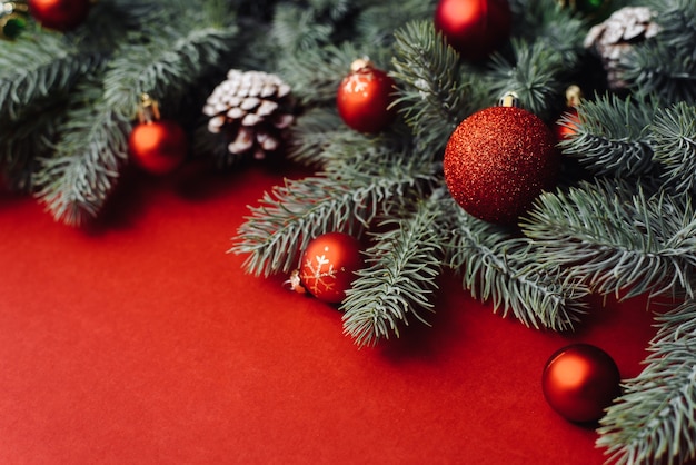 Space for text between Christmas tree branches with Christmas decorations and balls on a red background.