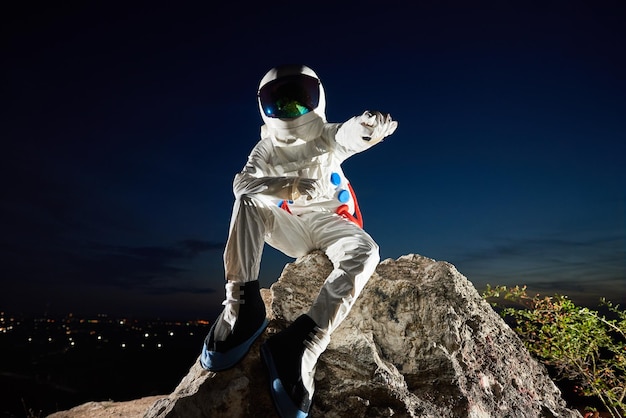 Space traveler sitting on rocky mountain under night sky