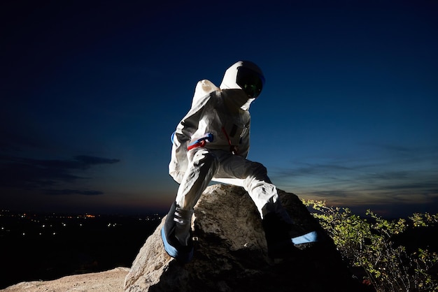 Spaceman sitting on rocky mountain under beautiful blue sky