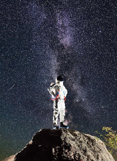 Photo spaceman standing on rocky mountain under starry sky