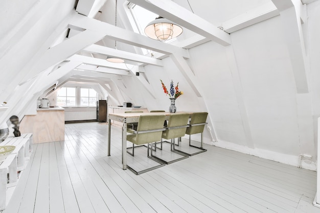 Spacious attic room of apartment with dining table and chairs near open kitchen under roof with beams