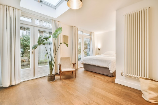 A spacious bright bedroom with a large white bed and a small armchair next to it on the parquet floor of a modern house