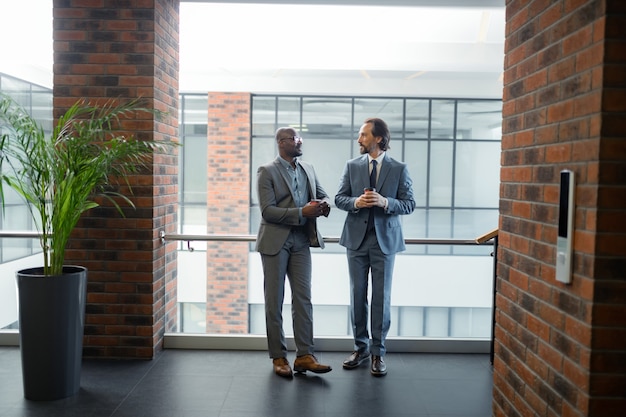 Spacious business center. Two businessmen standing in spacious business center in the morning and drinking coffee