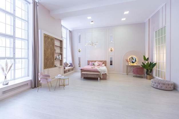 Spacious expensive luxury bright interior of open-plan apartment in pink colors with dressing room, bedroom area and cozy area for guests with soft furniture. fashionable LED lighting and huge windows