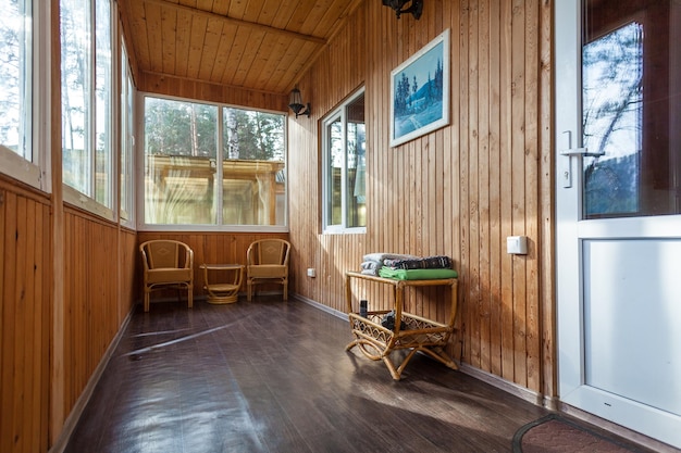 A spacious furnished corridor in a woodenstyle cottage with a large windows chairs and decoration