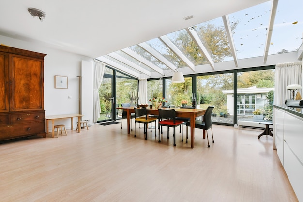 Spacious mansion kitchen room with glass walls and ceiling above wooden dining table in daylight