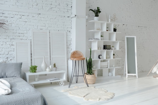 Spacious stylish modern trendy loft apartment in white and gray colors full of sunlight. brick wall, shelving, pallet bed and teepee-shaped children's house.