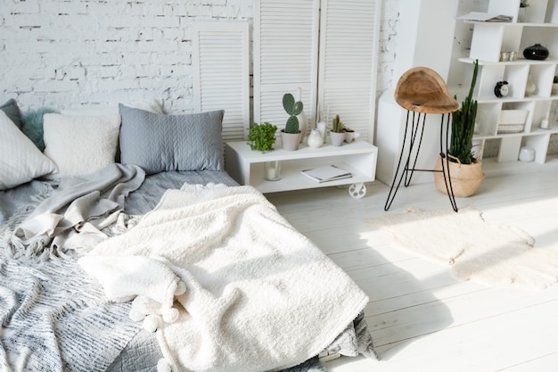 Spacious stylish modern trendy loft apartment in white and gray colors full of sunlight. brick wall, shelving, pallet bed