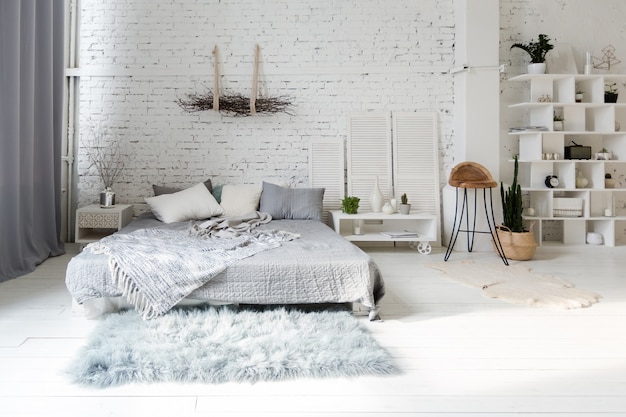 Spacious stylish modern trendy loft apartment in white and gray colors full of sunlight. brick wall, shelving, pallet bed