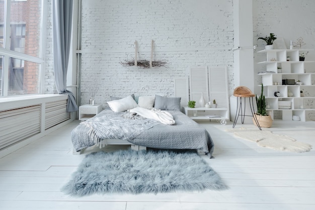 Spacious stylish modern trendy loft apartment in white and gray colors full of sunlight. brick wall, shelving, pallet bed