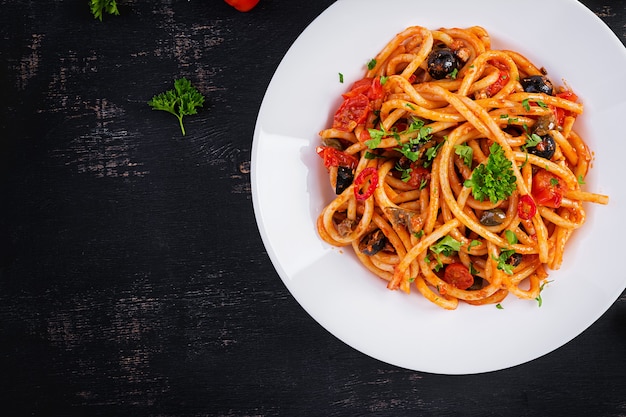 Spaghetti alla puttanesca - piatto di pasta italiana con pomodori, olive nere, capperi, acciughe e prezzemolo. vista dall'alto, posizione piatta