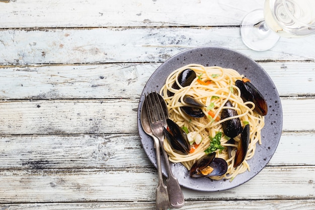 Spaghetti allo scoglio, pasta met zeevruchten, mosselen op een grijze keramische plaat over houten