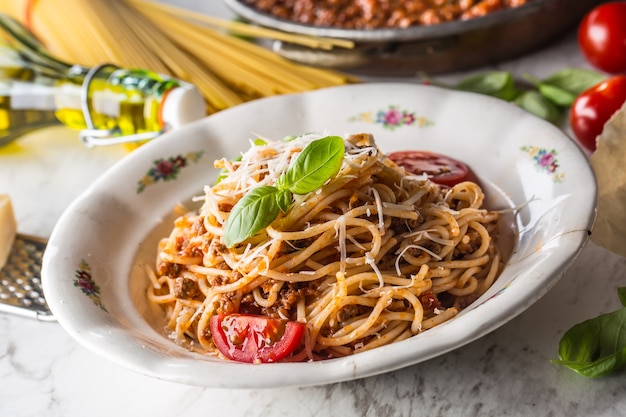 Spaghetti bolognese met ingrediënten basilicum tomaten Parmezaanse kaas en olijfolie.