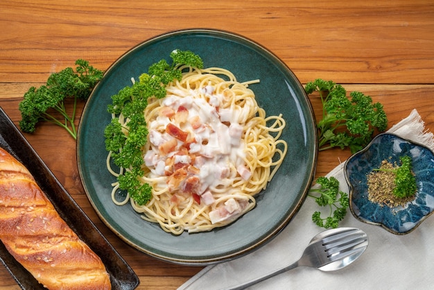 Spaghetti alla carbonara con prosciutto e pancetta sulla zolla verde sulla tavola di legno