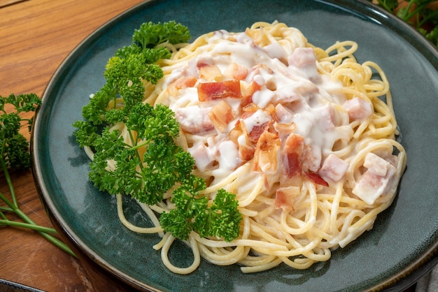 Spaghetti alla carbonara con prosciutto e pancetta sulla zolla verde sulla tavola di legno