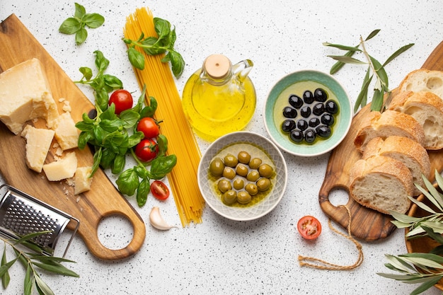 Spaghetti, cheese parmesan, ripe olives, ciabatta, olive tree sprigs and snacks on white rustic background. Ingredients and appetizers for Italian pasta or mediterranean healthy meal, top view