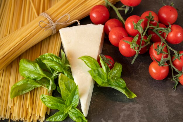 Spaghetti on a dark background, cheese, tomatoes, and basil