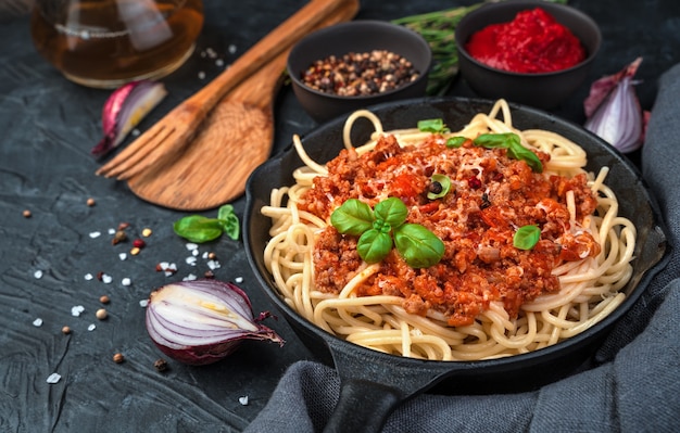 Spaghetti en saus in een koekenpan worden bestrooid met kaas en verse basilicum op een achtergrond van