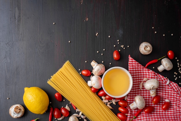 Spaghetti ingredients on black wooden desk, top view.