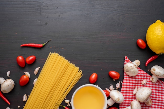 Spaghetti ingredients on black wooden desk, top view.