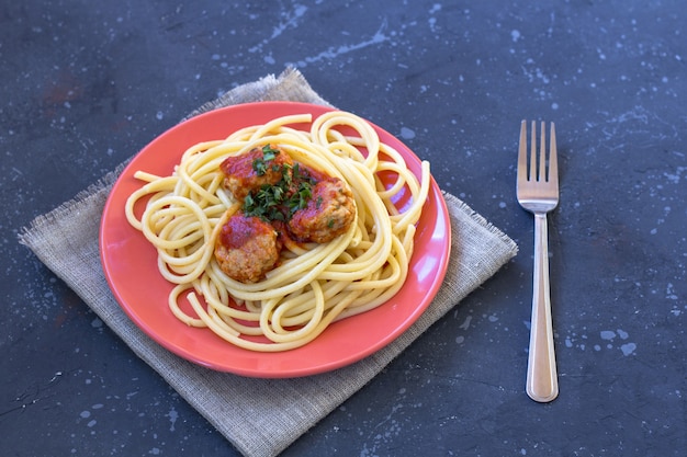 Spaghetti met gehaktballetjes en tomatensaus in een rode plaat