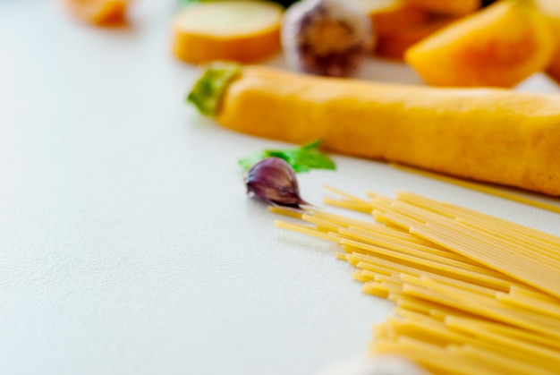 Spaghetti met gele courgette, tomaat, knoflook, champignon, peterselie op witte achtergrond plat lag