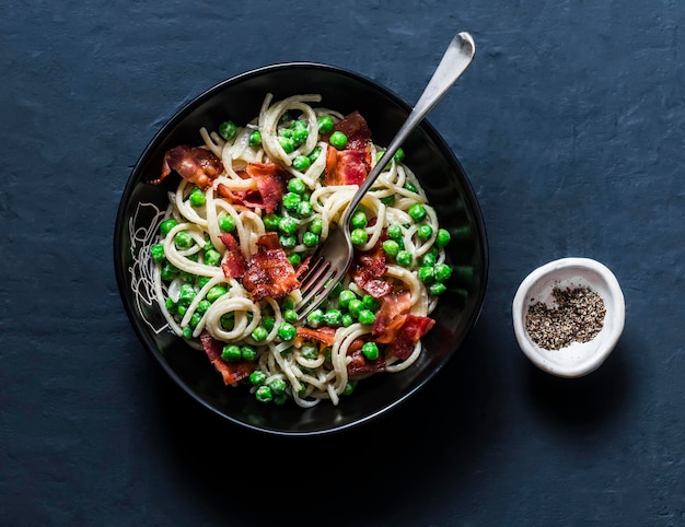 Spaghetti met spek en romige groene erwten op een donkere achtergrond bovenaanzicht