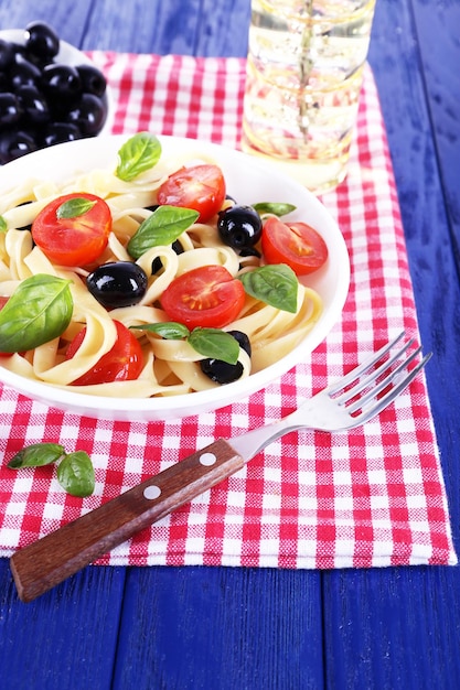 Spaghetti met tomatenolijven en basilicumbladeren op plaat op servet op houten achtergrond