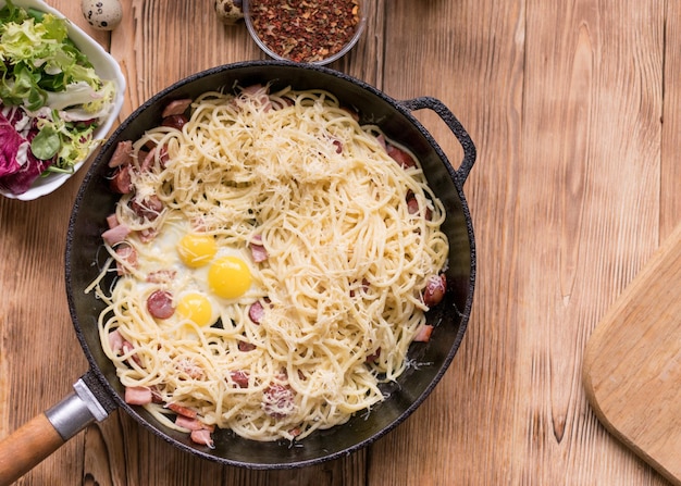 Spaghetti met worstjes kaas en kwarteleitjes in een koekenpan