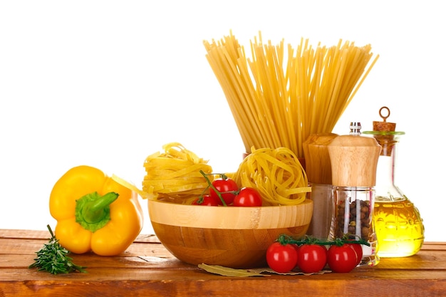 Spaghetti noodles in bowl jar of oil and vegetables on wooden table isolated on white