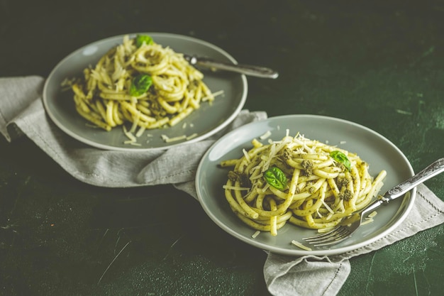 Spaghetti pasta bucatini with pesto sauce and parmesan Italian traditional perciatelli pasta by genovese pesto sauce in two gray dishes