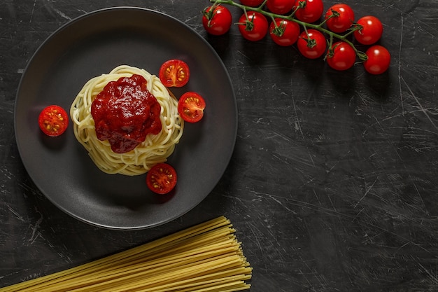 Spaghetti pasta gekookt met tomatensaus op een grijze plaat ingrediënten rauwe pasta cherrytomaatjes bovenaanzicht donkere achtergrond met ruimte om tekst te kopiëren