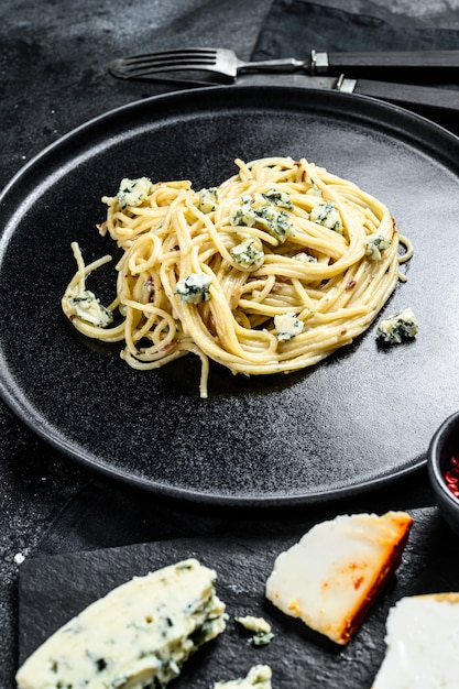 Spaghetti pasta met blauwe Gorgonzola kaassaus. Zwart oppervlak. Bovenaanzicht.