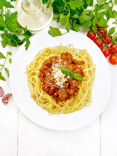 Spaghetti pasta met bolognese saus van gehakt, tomatensap, knoflook, wijn en kruiden met kaas in een bord, plantaardige olie, pittig kruid op een lichte houten plank achtergrond van bovenaf