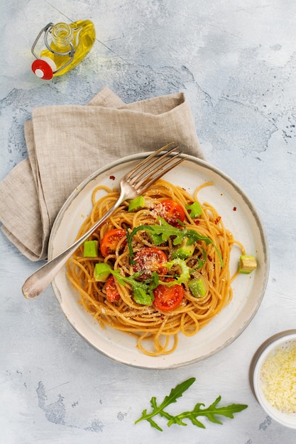 Spaghetti pasta met pesto, avocado en tomaten in rustieke witte plaat. Rauw veganistisch voedselconcept. Bovenaanzicht.